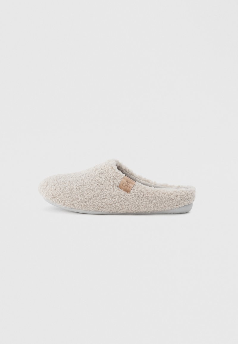 Beige pantoffel met een gestructureerde, fuzzy buitenkant, instapontwerp en een klein leren accentlabel aan de zijkant. Zachte voering en rubberen zool.