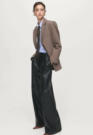 Brown checkered blazer over a light blue shirt, paired with wide black faux leather trousers and brown pointed shoes. Gold stud earrings included.
