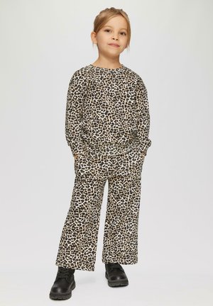 Beżowo-brązowy zestaw odzieży loungewear w cętki; charakteryzuje się luźnym krojem, długimi rękawami i elastycznymi mankietami. W zestawie czarne buty sznurowane.