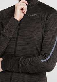Svart texturerad zip-up jacka med hög krage, med reflekterande grå detaljer på ärmarna och "CRAFT"-logotypen på bröstet.