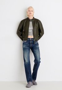 Chaqueta de cuero verde oliva, top corto gris, jeans rectos azul oscuro y zapatillas grises. El conjunto presenta un diseño minimalista.