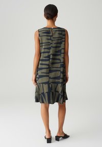 Sleeveless dress in olive green with abstract navy patterns. Features a back button closure and a flared hem for a relaxed fit.