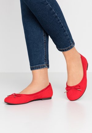 Røde ballerinaer i ruskind med rundet tå, dekorativ sløjfe foran og lav flad sål, kombineret med mørkeblå ankellange jeans.