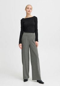 Top negru cu manșon lung și textură cu nervuri, asortat cu pantaloni gri în carouri cu picioare largi. Îmbrăcămintea prezintă o siluetă elegantă și cizme negre elegante.