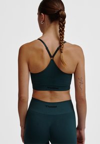 Donkergroene sportbeha met een racerback-ontwerp, verstelbare bandjes en gebrandmerkte tekst. Bijpassende hoge taille legging zichtbaar daaronder.