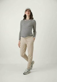 Jūras un baltas svītraina garām piedurknēm krekls, kombinēts ar bēša sporta biksēm. Pelēka cepure un sportiskās kedas noslēdz izskatu.