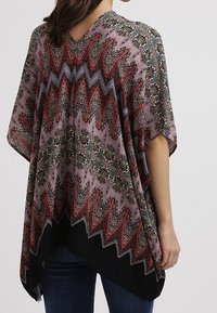 Flerfärgad poncho med ett zigzag-mönster, försedd med en blommig design i rosa, rött och grönt. Tillverkad av lättviktsmaterial med V-ringning.