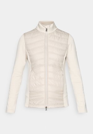 Veste zippée légère de couleur crème, avec un devant matelassé à coutures horizontales, des manches lisses, un col montant et deux poches latérales.