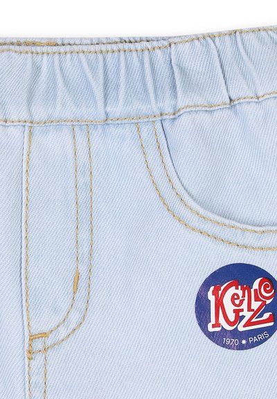 Tissu en denim bleu clair avec une taille élastique, des coutures jaunes, et un patch logo circulaire rouge et bleu portant l'inscription "Kenzo 1970 Paris."