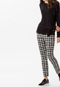 Pull noir avec un détail froncé sur le côté, associé à un pantalon ajusté noir et blanc à motif pied-de-poule et des baskets noires.