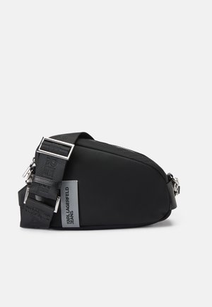 Sac à bandoulière noir en nylon avec une forme courbée, bandoulière réglable, quincaillerie en métal et un patch logo. Texture lisse avec fermeture éclair.