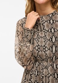 Genomskinlig klänning med ett ormskinsmönster i beige och brunt. Har smockade ärmslut och en avslappnad passform som framhäver det texturerade tyget.
