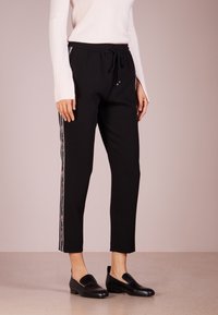 Zwarte sportbroek met een trekkoord in de taille, voorzien van zijaccenten met bloemen en een cropped zoom. Gecombineerd met zwarte instappers.