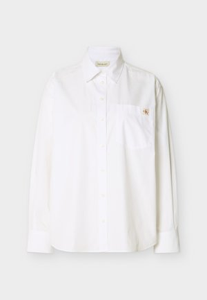Λευκό μακρυμάνικο πουκάμισο από βαμβάκι. Διαθέτει μυτερό γιακά, κουμπιά μπροστά, τσέπη στην αριστερή πλευρά του στήθους και μικρό κεντημένο λογότυπο.