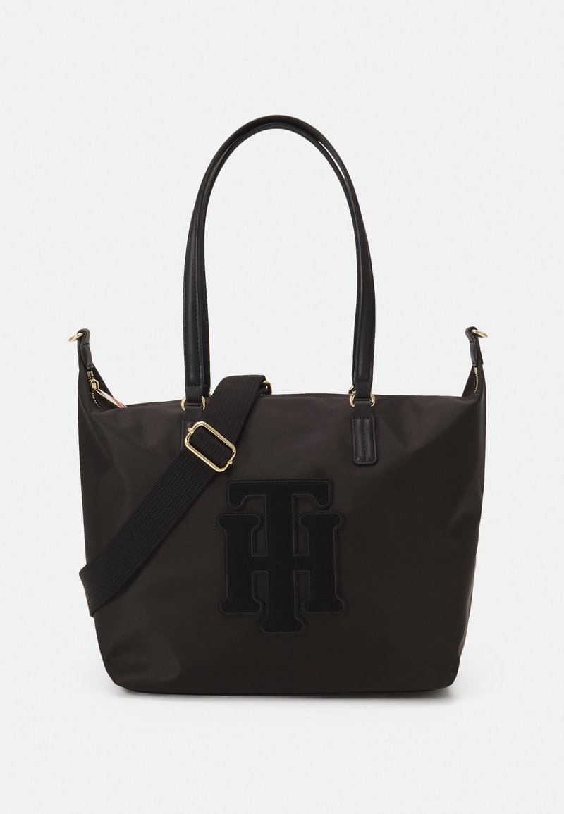 Black tote bag made of durable fabric, featuring dual handles, an adjustable strap, and textured logo detail on the front. Gold hardware accents.