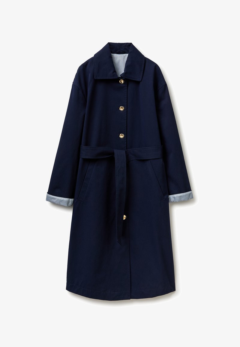Long manteau bleu marine avec boutons dorés, ceinture assortie, poches latérales et doublures de poignets rayées bleu et blanc.