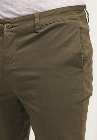 Chinos khaki con una vestibilità slim, realizzati in cotone leggero, dotati di una parte anteriore piatta, tasche laterali e chiusura a un solo bottone.