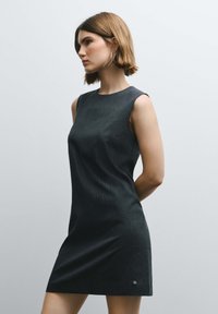 Temno siva obleka brez rokavov z navpičnimi črtami, oprijetim krojem, okroglim izrezom in subtilnim logotipom na robu. Gladek tekstura.