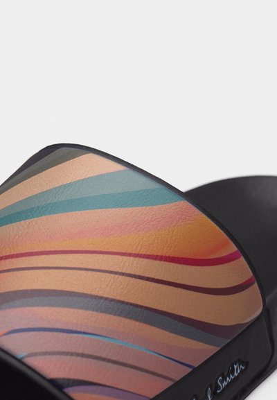 Κοντινό πλάνο λουριού σανδαλιού με πολύχρωμες κυματιστές ρίγες σε αποχρώσεις μπεζ, μπλε, ροζ, πορτοκαλί και μωβ σε υλικό με υφή.