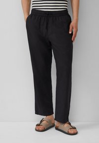 Pantalons noirs, légers et amples avec une taille élastique et un cordon de serrage. Associés à des sandales marron avec une détail de boucle.