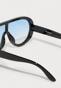 Černé sluneční brýle s oversized, hranatými rámy, které mají modré gradientové čočky a lesklý povrch. Na nožce je vytištěna značka "YOURTURN".