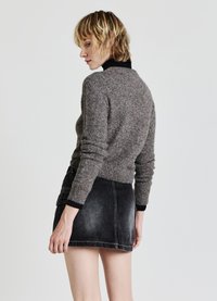 Young person with short blonde hair wears gray knit sweater over black turtleneck and black denim mini skirt, posing sideways.