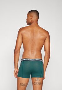 Green boxers with an elastic waistband featuring "JACK & JONES" in black text. The garment has a snug fit and smooth material.