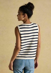 Gestreepte mouwloze trui in crème en marineblauw, gemaakt van een zachte textuurstof. Draagt met blauwe high-waisted jeans, die een casual pasvorm tonen.