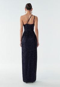 Dlhé nočné šaty s flitrami a priliehavým strihom, jedným nastaviteľným ramienkom a rovnou zadnou časťou. Hladká textúra s trblietavými detailmi po celom povrchu.