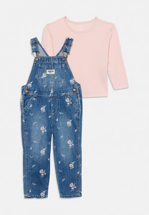 Chemise rose à manches longues associée à une salopette en jean bleu avec des bretelles réglables, des poches avant et un petit imprimé floral.
