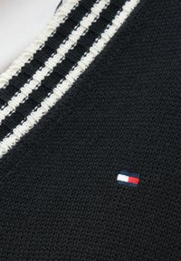 Črno pleteno blago z reliefno površino, z obrobom z belimi in črnimi črtami ter majhnim rdeče-belo-modrim logotipom.