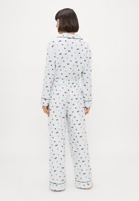 Lichtblauwe pyjama-set met een patroon van kleine bloemen en bladeren, lange mouwen en een elastische tailleband. Zwarte piping accenten.