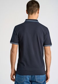 Marinbl å polo med kontrasterande vit och blårandig krage och ärmmuddar; gjord av ett mjukt tyg; figurnära design med sidslitsar vid fållen.