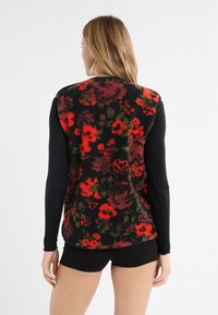 Czarna kamizelka z polaru w kwiaty, z czerwonym i zielonym wzorem kwiatowym, połączona z długimi czarnymi rękawami. Tkanina o fakturze z miękkim wykończeniem.