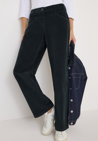 Pantalons en velours côtelé vert foncé avec une coupe droite, dotés d'une fermeture à bouton, de poches latérales et de détails de couture subtils.