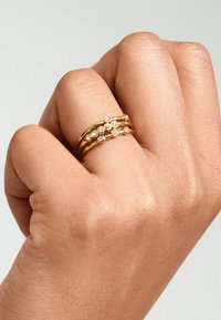 Gul rings med tre bånd, der skifter mellem glatte og strukturerede overflader, prydet med flere små klare ædelstene i et lineært mønster.