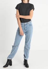 Tmavě šedé tričko s krátkým rukávem v kombinaci se světle modrými, vysoce pasovými roztrhanými džíny a černými kotníkovými botami. Ležérní a přiléhavý design s roztrhanými detaily.