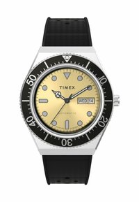 Timex automatic watch with a stainless steel case, black bezel, and gold dial. Features white hour markers, date display, and black rubber strap.