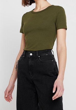 T-shirt vert olive à manches courtes en coton, avec un col rond et une coupe ajustée, associé à un jean en denim noir taille haute.
