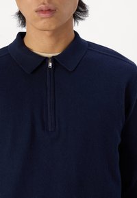 Maglione a maglia blu navy con colletto con zip, texture liscia e dettagli a costine sulle maniche e sul colletto. Design minimalista.