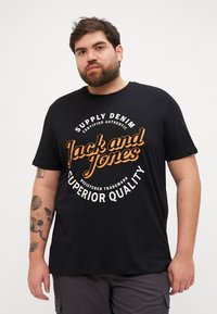 Svart bomull t-skjorte med sirkulært trykk som har "Jack and Jones" i oransje. Korte ermer, rund hals og en avslappet passform.