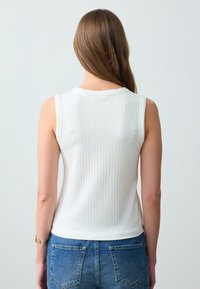 Witte, geribbelde mouwloze top met een ronde halslijn. De stof heeft een fijne textuur en het past mooi bij blauwe denim shorts.