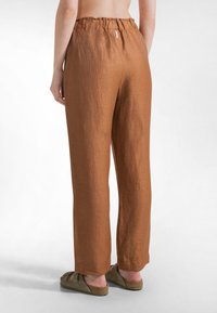Brune linnedbukser med afslappet pasform, elastisk talje og lige ben. Mærkbar tekstur og afsluttet med en kant ved anklerne.