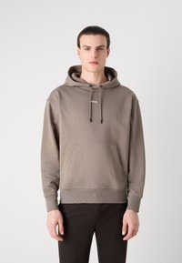 Sudadera con capucha en beige suave, con un bolsillo frontal, puños y dobladillo acanalados, y un pequeño logo blanco centrado en el pecho.