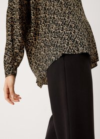 Blusa nera con un motivo astratto dorato, vestibilità ampia e maniche lunghe, abbinata a pantaloni neri a gamba stretta. Tessuto liscio con una consistenza morbida.