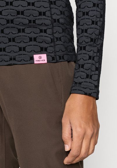 Melna ar garām piedurknēm augšdaļa ar paceltu brilles rakstu un rozā "FIRE + ICE" etiķeti apakšmalā. Kombinēts ar brūnām biksēm.