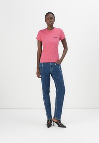 Roze katoenen t-shirt met korte mouwen en zwart logo, gecombineerd met blauwe denim jeans met zilveren zijaccenten en zwarte hakken.