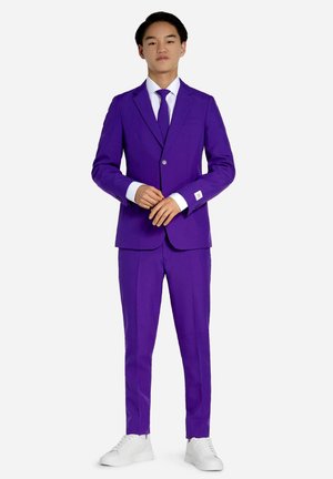 Costume violet avec une fermeture à un seul bouton, chemise blanche, cravate assortie et baskets blanches. Le tissu a une texture lisse.