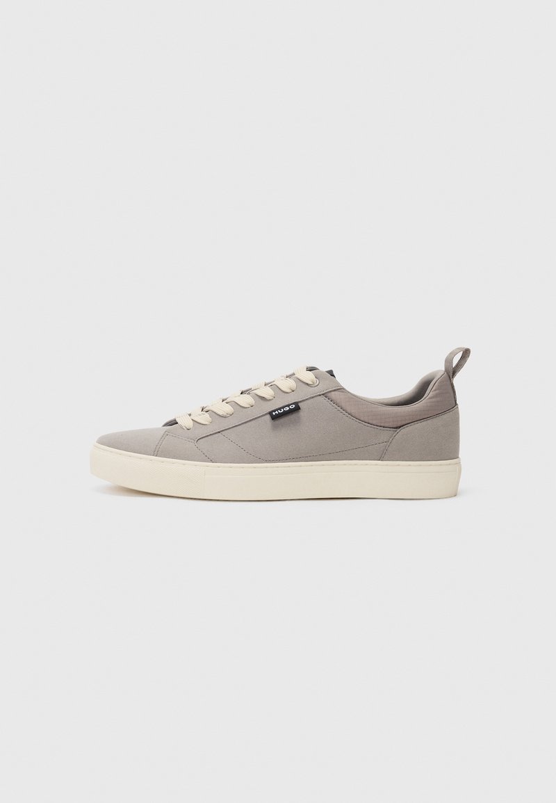 Gray canvas sneakers with a rounded toe, beige laces, and a contrasting beige rubber sole. Features a rear pull tab and brand label on the side.