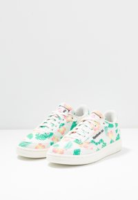 Sneaker con motivo floreale, con una parte superiore in tessuto bianco, caratterizzata da foglie verdi e fiori rosa, design con lacci e suola in gomma color crema.